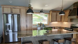 A modern kitchen with wooden cabinets, stainless steel appliances, and a large island with bar stools. - Spring special! Enjoy Lake Martin at its best! (Jacksons Gap)