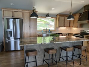 A modern kitchen with wooden cabinets, stainless steel appliances, and a large island with bar stools. - Spring special! Enjoy Lake Martin at its best! (Jacksons Gap)