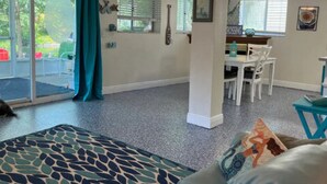 Un salón espacioso con ventilador de techo, una mesa de comedor con sillas y un gran ventanal con persianas.