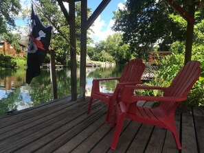 A wooden deck with two red chairs and a flag. - The Mermaid Landing River Retreat (Weeki Wachee)