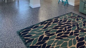Amplia sala de estar con una cocina al fondo, una mesa de comedor con sillas y una alfombra estampada.