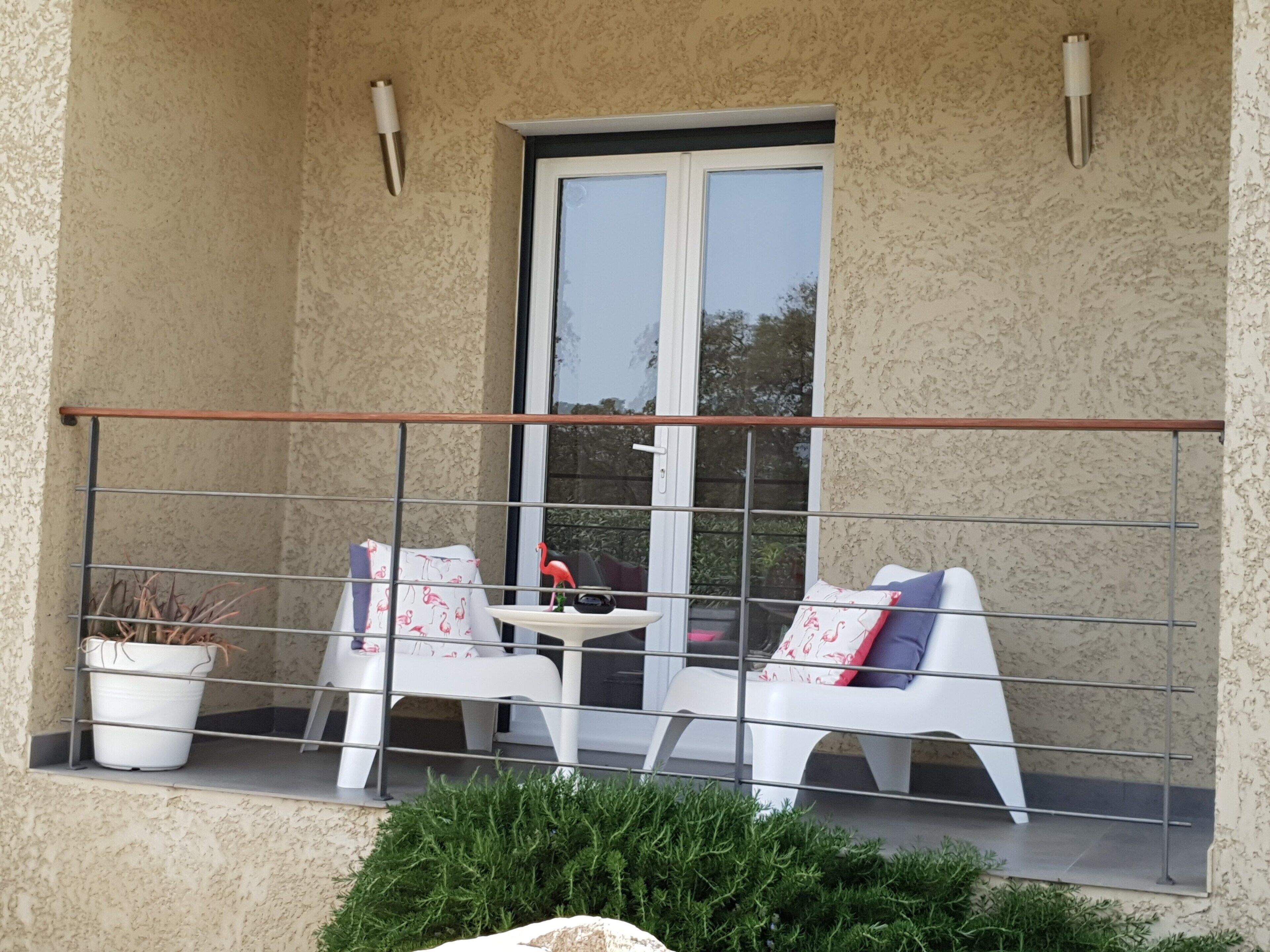 Un balcon avec deux chaises blanches, une petite table et un pot de fleurs.