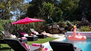 Un espace aménagé au bord de la piscine, avec des chaises longues, un flotteur en forme de flamant rose et un parasol rouge.