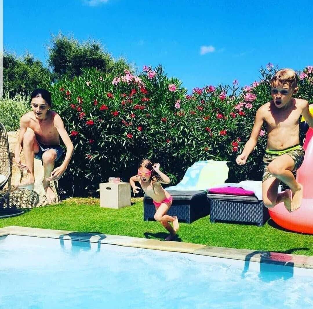 Ein Poolbereich mit blauem Himmel, Grünpflanzen und einer Liege.