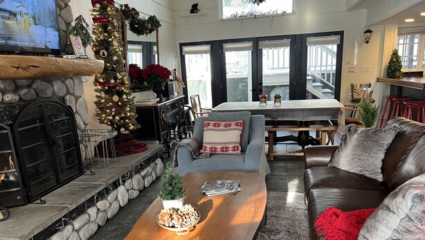 A cozy living room with a fireplace, a stone fireplace surround, a large grey sofa, a wooden coffee table with snacks, and a Christmas tree. - Steps to Bear Mountain & Golf Course Spacious 4BR Prime Moonridge Location (Big Bear Lake)