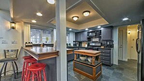 A modern kitchen with a bar area, red bar stools, and a central island with a bowl. - Steps to Bear Mountain & Golf Course Spacious 4BR Prime Moonridge Location (Big Bear Lake)