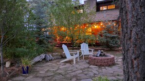 Un patio al aire libre con sillas Adirondack, un brasero y luces colgantes.