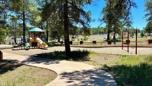 Un parque infantil con toboganes y columpios, rodeado de árboles y un cielo despejado.