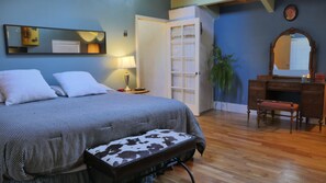 Ein Schlafzimmer mit Bett, Nachttisch, Lampe, Kommode, Spiegel und einer Bank.