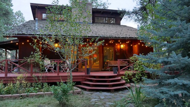 Una cabaña rústica con terraza de madera, mobiliario exterior y un camino de piedra que conduce a la entrada.