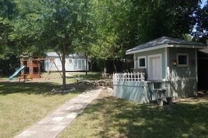 A fenced play area with a slide and swings, a small shed, and a pathway.