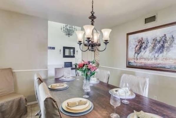 A dining area with a wooden table set for four, a chandelier, and a painting on the wall.