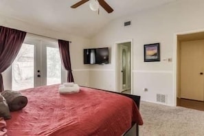 A bedroom with a bed, a television, and a door leading to another room.