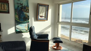 A living room with a view of the ocean, a black leather sofa, a glass coffee table, and artwork on the walls. - 3 *** FEET IN THE WATER, FACING THE SEA, access to the Beach,  F3 BRETAGNE SUD (Clohars-Carnoët)