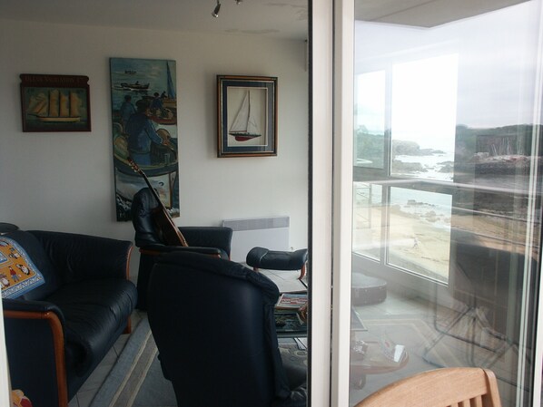 A living room with a black leather sofa, a violin, and framed paintings on the wall. - 3 *** FEET IN THE WATER, FACING THE SEA, access to the Beach,  F3 BRETAGNE SUD (Clohars-Carnoët)