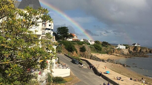 A coastal area with a road leading to a beach, a rainbow in the sky, and buildings in the background. - 3 *** FEET IN THE WATER, FACING THE SEA, access to the Beach,  F3 BRETAGNE SUD (Clohars-Carnoët)