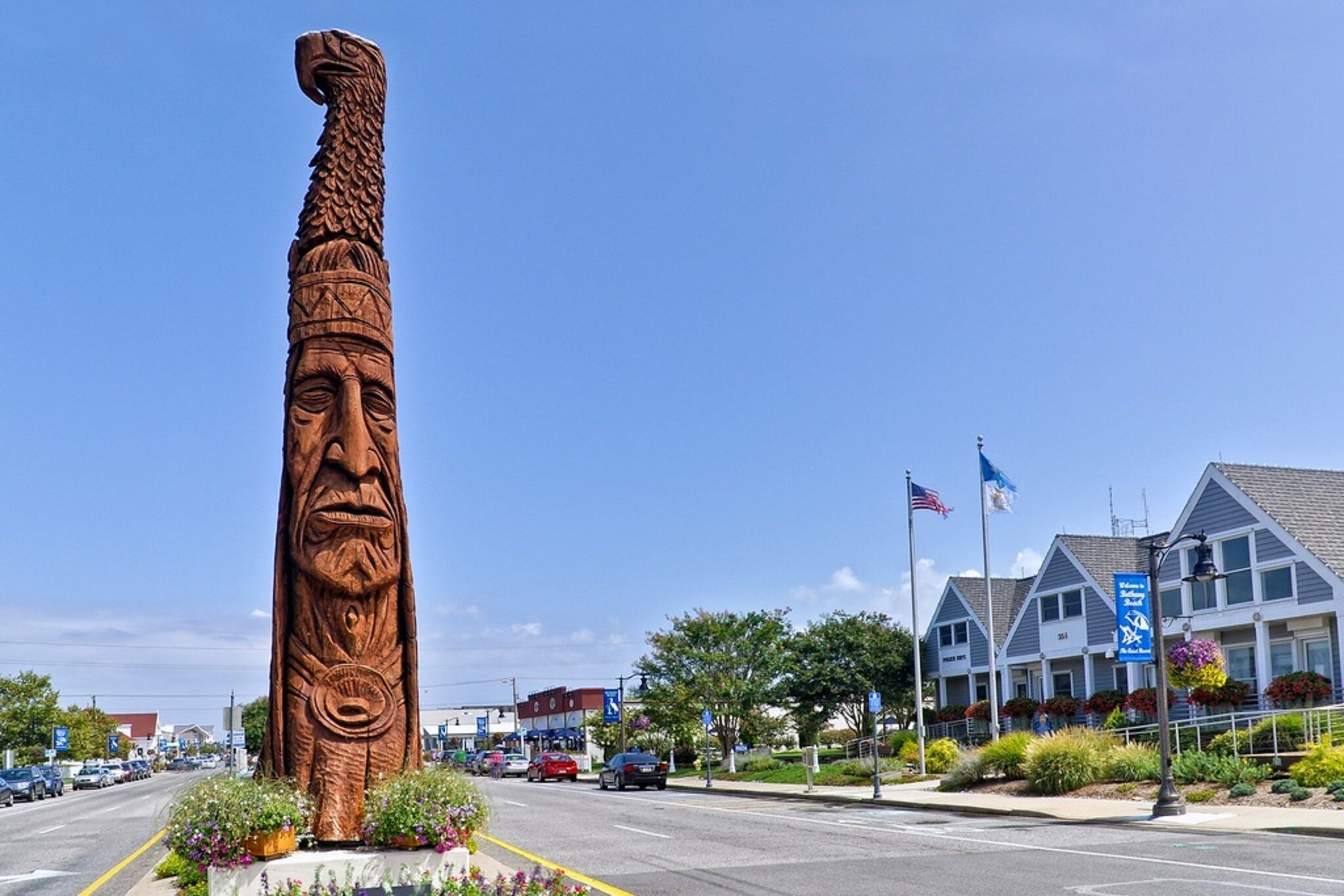 A large wooden totem with intricate carvings, a road with cars, and a building with flags and a sign.