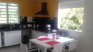A compact kitchen with white cabinets, a black range hood, and a window with a view of greenery. - ABC HOME BEAUTY HEAT !!!!!!!!!!!!!!!! (Le Gosier)