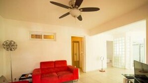 A spacious living room with a red sofa, a ceiling fan, and a TV. - ABC HOME BEAUTY HEAT !!!!!!!!!!!!!!!! (Le Gosier)