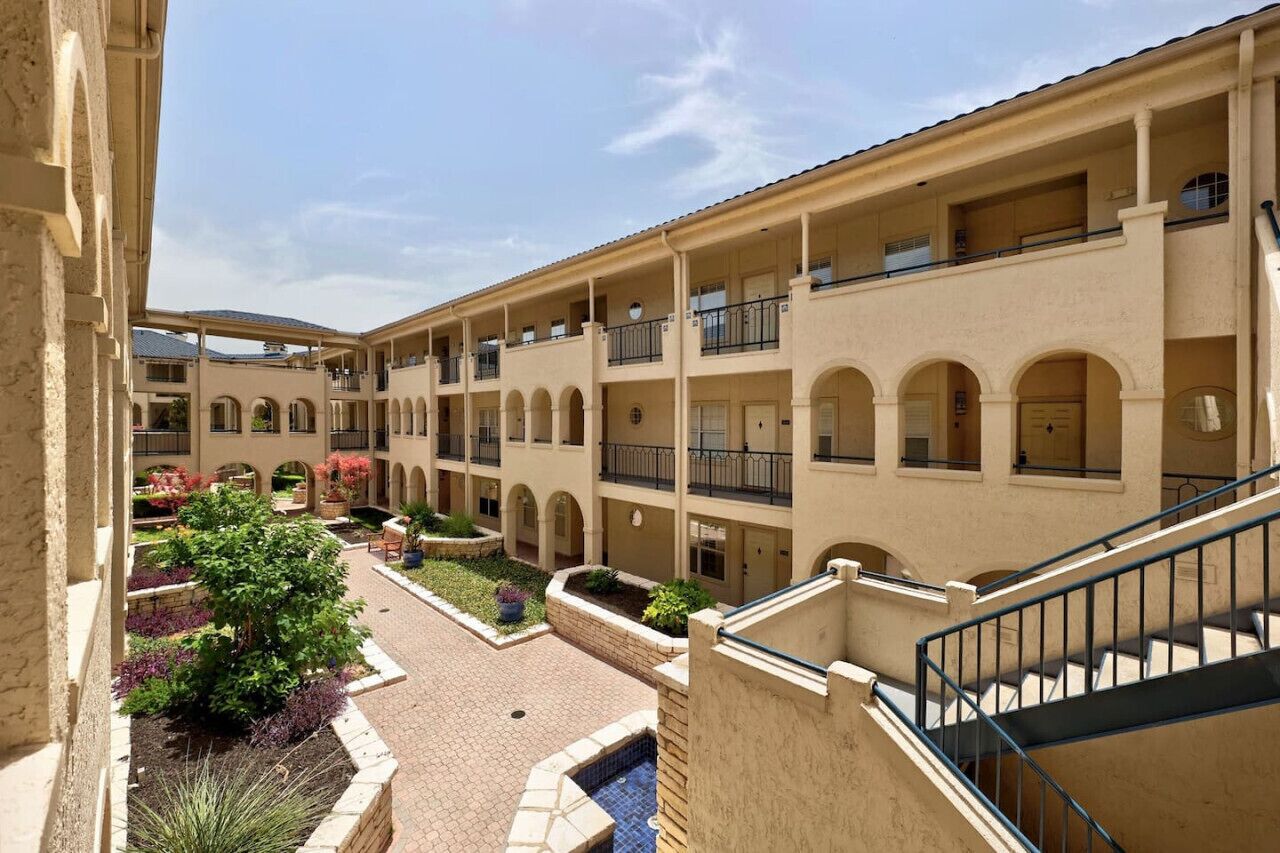 A multi-story building with balconies, a courtyard with plants, and a pool area.