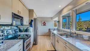 A modern kitchen with granite countertops, stainless steel appliances, and a large window offering a view of trees.