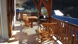 Terraza de madera con mesa y sillas, una parrilla y vistas a un cuerpo de agua.