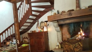 Una sala de estar acogedora con chimenea, una escalera de madera y un comedor con mesa lista para cuatro.