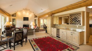 A spacious living area with a fireplace, a dining table with chairs, a kitchen with wooden cabinets, and a red patterned rug. - Luxury Family Retreat. Ski-in Ski-Out.  Spectacular Mountain Views.  Sleeps 12  (Snowmass Village)