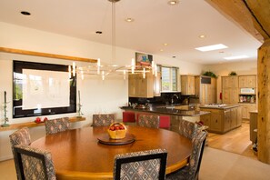 Cozinha moderna com armários de madeira, uma ilha central e uma área de refeições com mesa redonda e cadeiras estampadas.