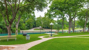 Un parc avec un sentier pédestre, des bancs, une poubelle et un étang.