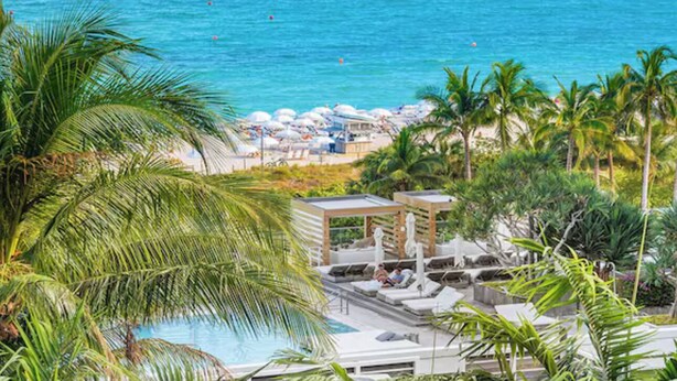 Un complexe hôtelier doté d’une piscine, de chaises longues et d’une plage aménagée avec des parasols.
