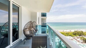 Un balcon doté de meubles en osier, d’une porte vitrée et offrant une vue sur la plage et l’océan.