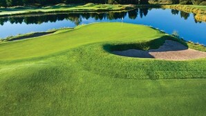 Un campo de golf con un estanque, búnkeres de arena y una bandera en el green.