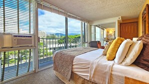 A hotel room with a large bed, a view of the cityscape, and a balcony with a railing.