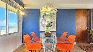 Un comedor con una mesa de vidrio, sillas anaranjadas, un jarrón decorativo y un cuadro en la pared.