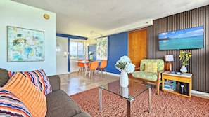 A modern living room with a sofa, coffee table, and a television. There's a dining area with chairs and a table.