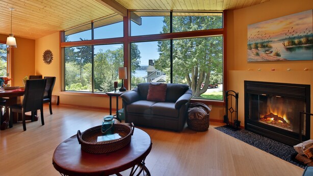 A spacious living room with a fireplace, large windows, and a cozy seating area. - Sun-filled Home with Stunning Deck and Two Cozy Fireplaces  (Freeland)