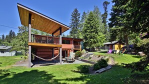 A modern two-story house with a wooden deck, a hammock, and a picnic table in the yard. - Sun-filled Home with Stunning Deck and Two Cozy Fireplaces  (Freeland)