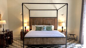 Ein Bett mit Baldachin, ein hölzernes Kopfende, zwei Nachttische mit Lampen, ein karierter Boden und ein gemustertes Teppich.