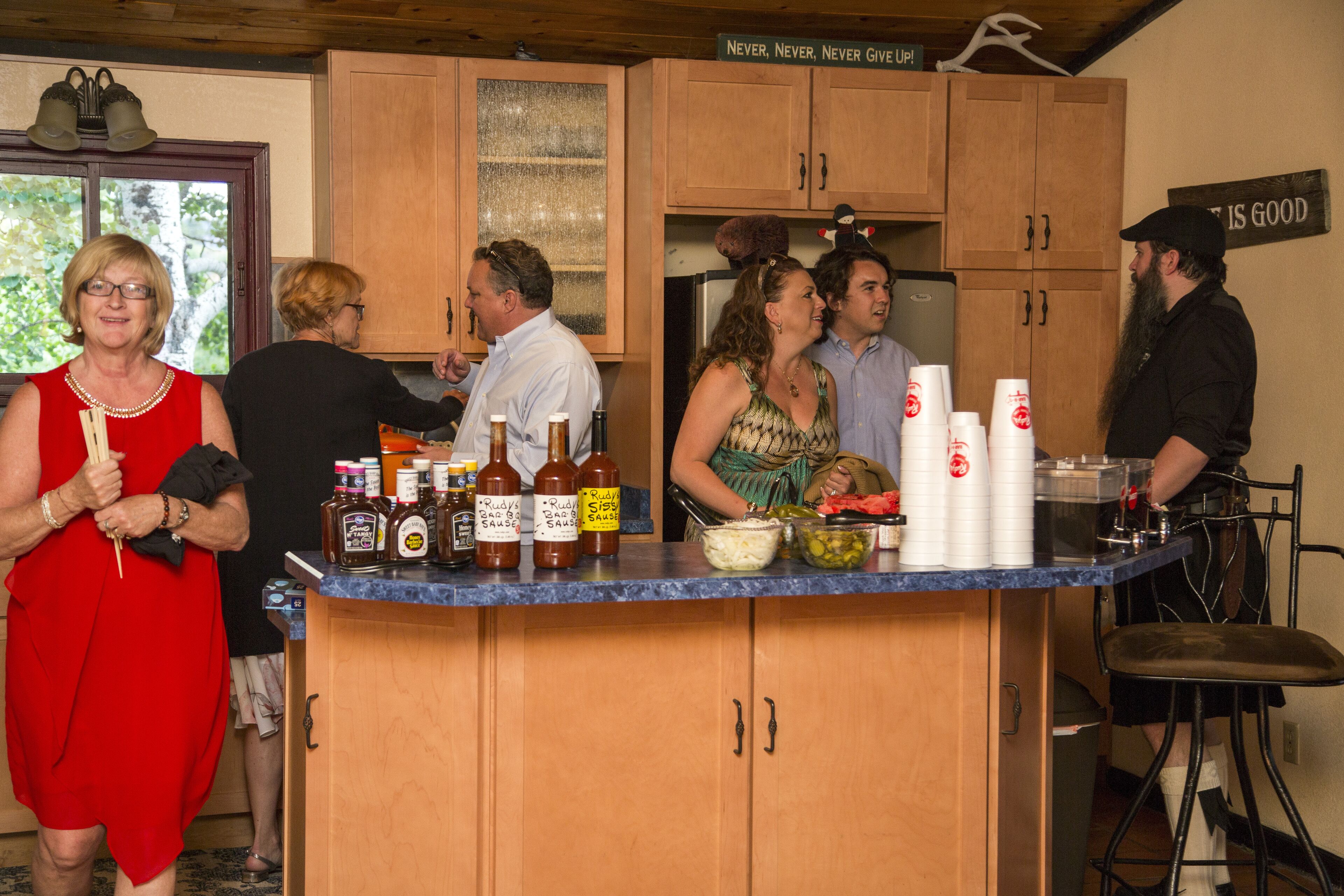A kitchen with wooden cabinets, a countertop with various food items and condiments, and a sign on the wall.