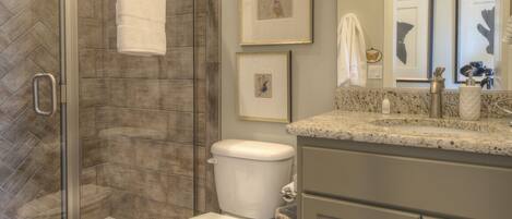 A bathroom with a glass-enclosed shower, a toilet, and a vanity with a mirror.