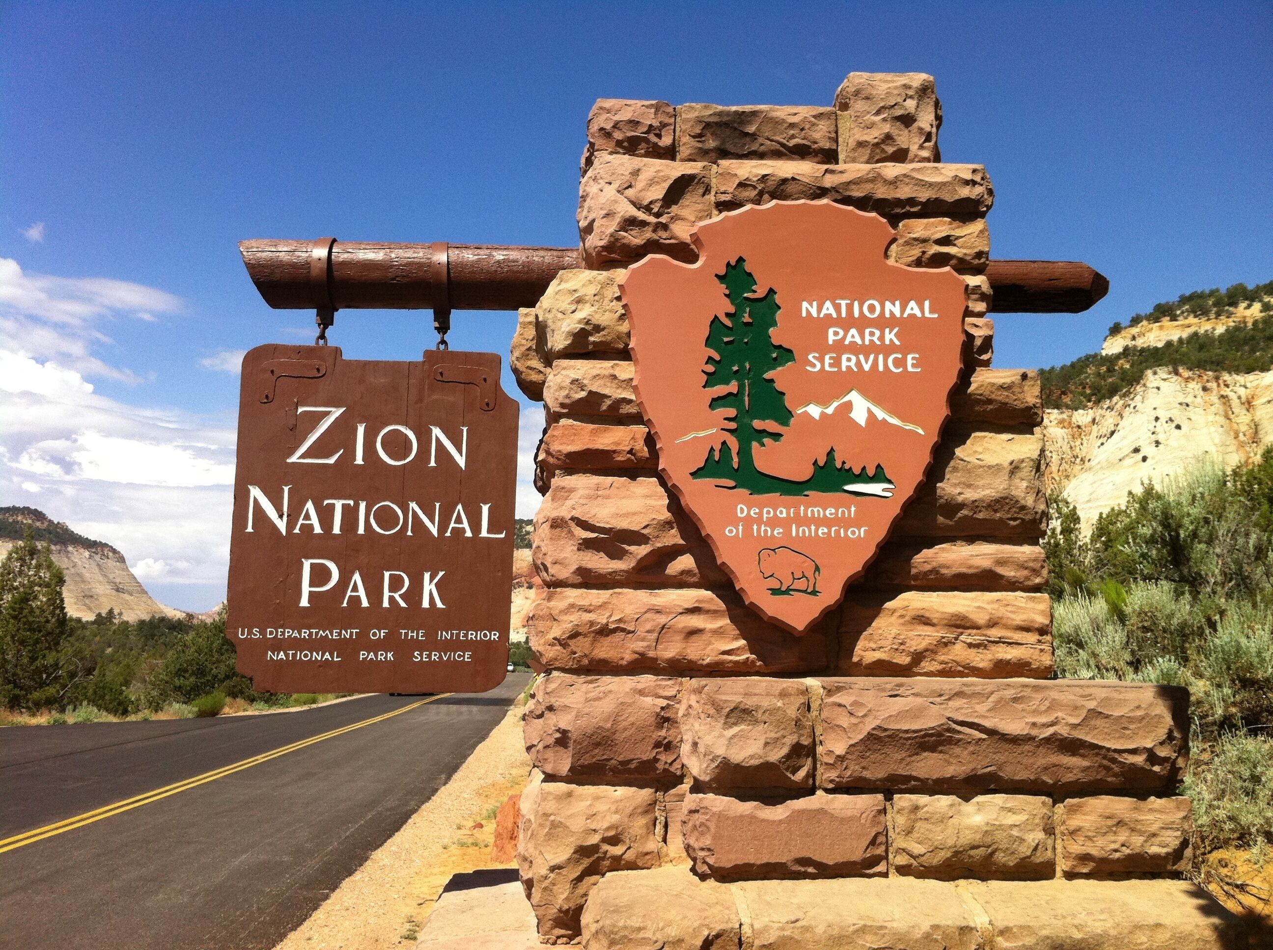 A road sign for Zion National Park with a stone wall backdrop.