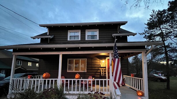 Une maison avec un porche décoré de citrouilles et orné d’un drapeau américain.