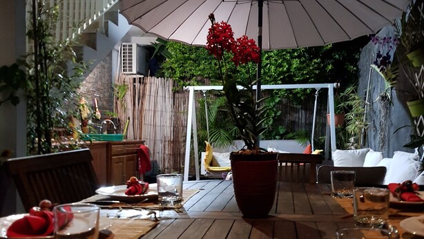 Een buitenterras met een tafel gedekt voor twee personen, een plant in pot en een grote parasol voor schaduw.