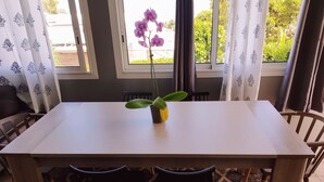 Een eethoek met een tafel, stoelen, een potplant en een raam met gordijnen.