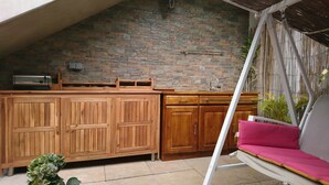 Een keuken met houten kastjes, een betegelde achterwand en een hangstoel met een roze kussen.