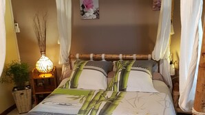 Een bed met een bedspreide in bamboestijl, een bedlampje en een kleine potplant.