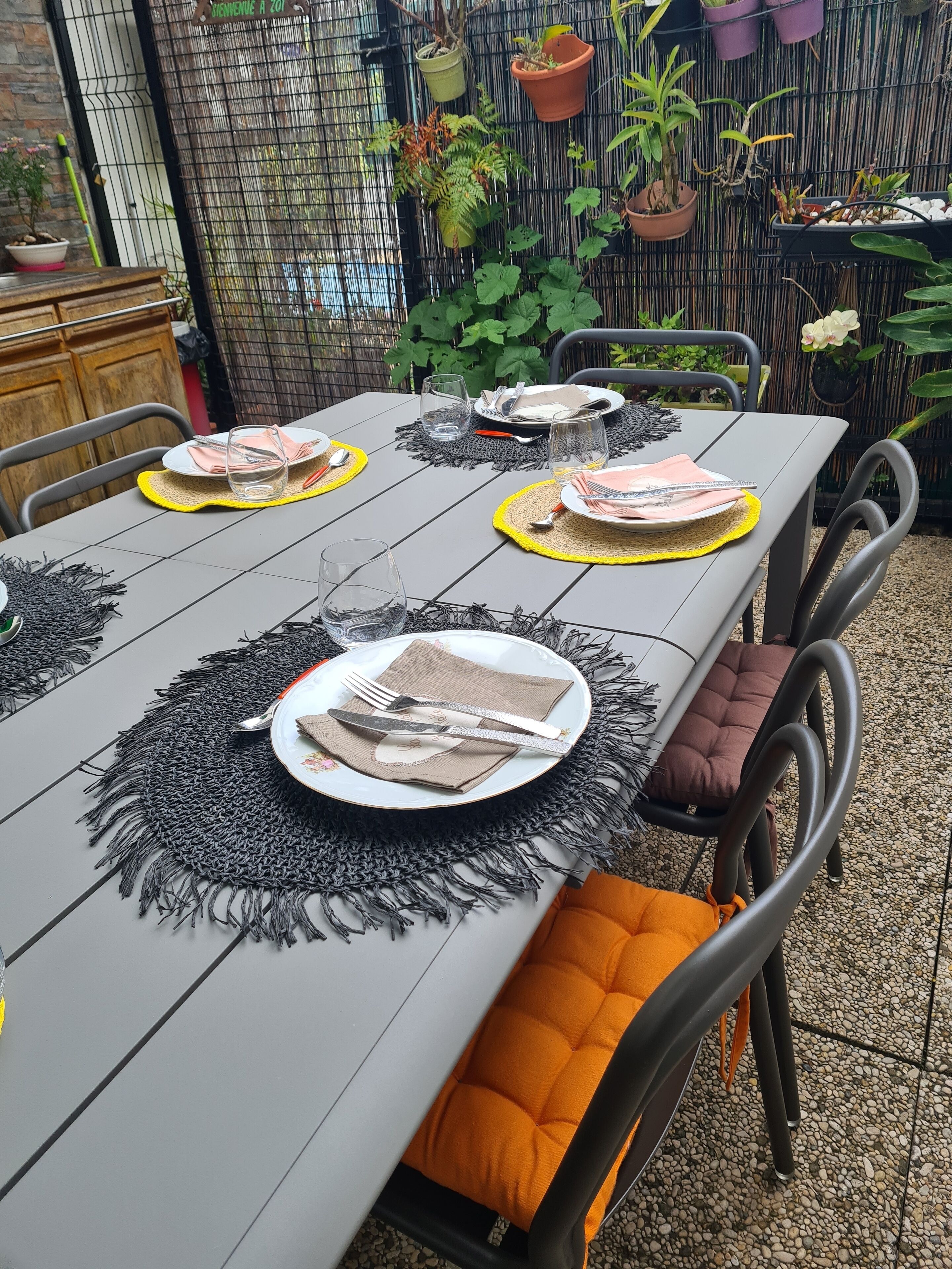 A dining table set with plates, cutlery, and napkins, surrounded by chairs with orange cushions.