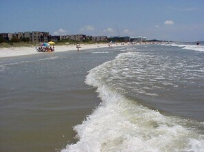 A beach with a sandy shore, waves, and buildings in the background.