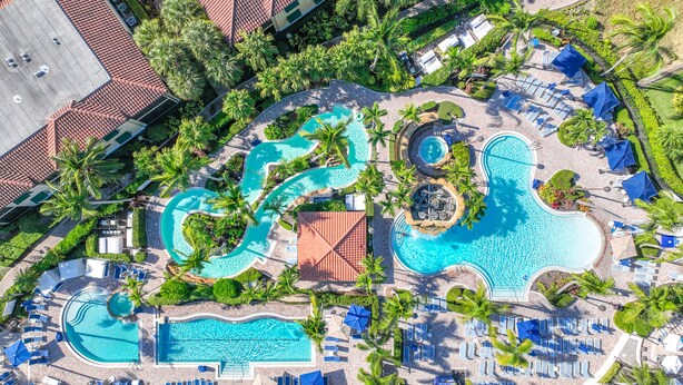 Vista aérea de un resort con múltiples piscinas, tumbonas y palmeras.